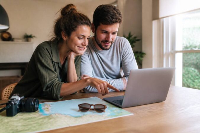 Een realistische foto van een stel dat op een laptop vakantieopties vergelijkt met een kaart en notities op tafel